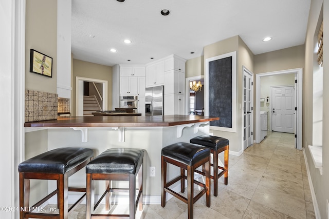 kitchen featuring stainless steel fridge with ice dispenser, kitchen peninsula, washer / dryer, a breakfast bar, and white cabinets