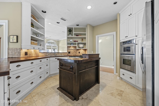 kitchen featuring butcher block counters, stainless steel appliances, tasteful backsplash, a textured ceiling, and white cabinets