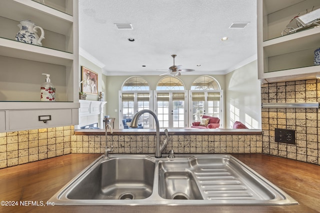 kitchen with a textured ceiling, ornamental molding, sink, and tasteful backsplash