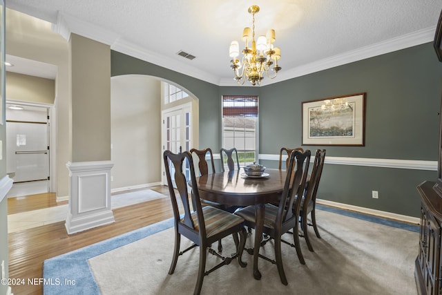 dining area with hardwood / wood-style floors, crown molding, a textured ceiling, a notable chandelier, and decorative columns