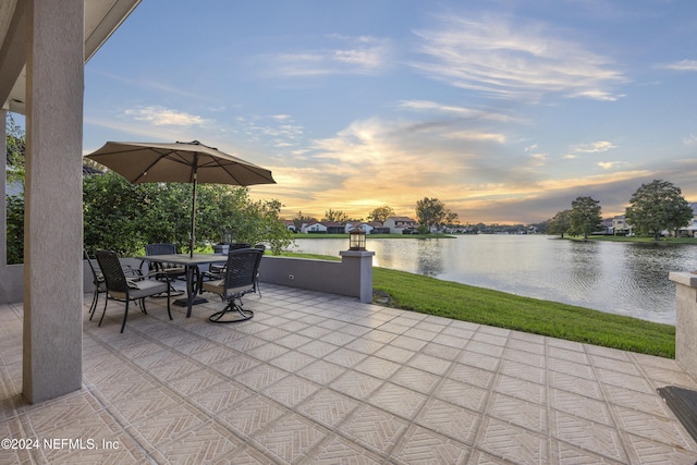 patio terrace at dusk featuring a water view and a yard