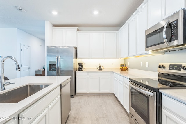 kitchen with appliances with stainless steel finishes, light wood-type flooring, light stone counters, sink, and white cabinetry