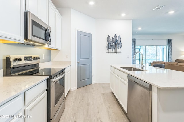 kitchen with a kitchen island with sink, sink, light wood-type flooring, appliances with stainless steel finishes, and white cabinetry