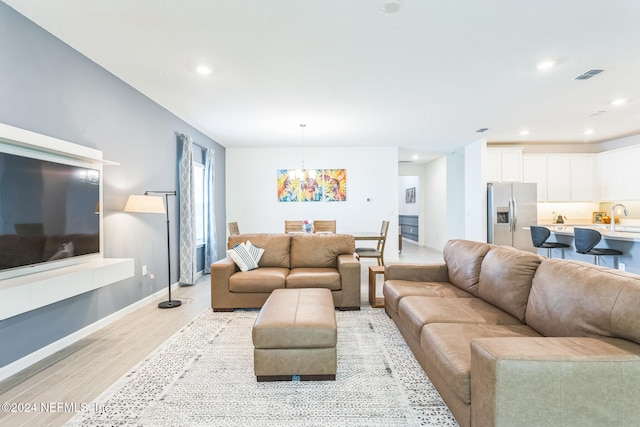 living room with sink, light hardwood / wood-style floors, and a notable chandelier