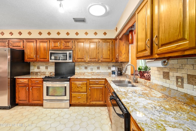 kitchen featuring tasteful backsplash, a textured ceiling, stainless steel appliances, sink, and light tile patterned floors