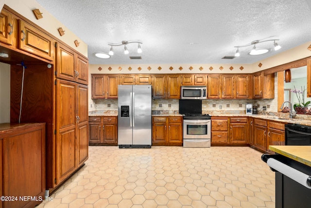 kitchen with track lighting, tasteful backsplash, a textured ceiling, stainless steel appliances, and sink