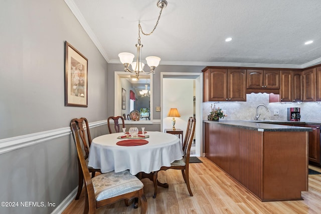 dining space featuring a notable chandelier, light hardwood / wood-style floors, ornamental molding, and a textured ceiling