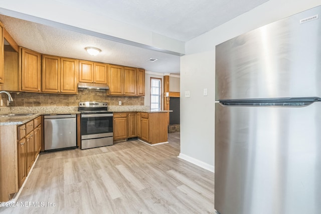 kitchen featuring light stone countertops, appliances with stainless steel finishes, tasteful backsplash, sink, and light hardwood / wood-style floors