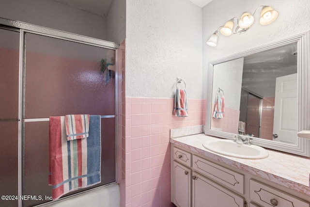 bathroom featuring tile walls, enclosed tub / shower combo, and vanity