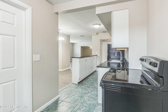 kitchen with kitchen peninsula, electric range, white cabinetry, and sink