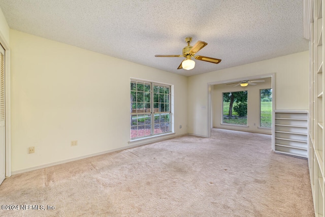 empty room with a textured ceiling, light colored carpet, and ceiling fan