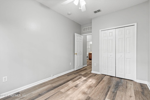 unfurnished bedroom with a textured ceiling, hardwood / wood-style floors, ceiling fan, and a closet