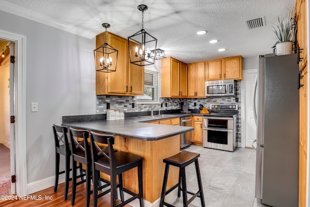 kitchen featuring kitchen peninsula, appliances with stainless steel finishes, sink, hanging light fixtures, and a breakfast bar area