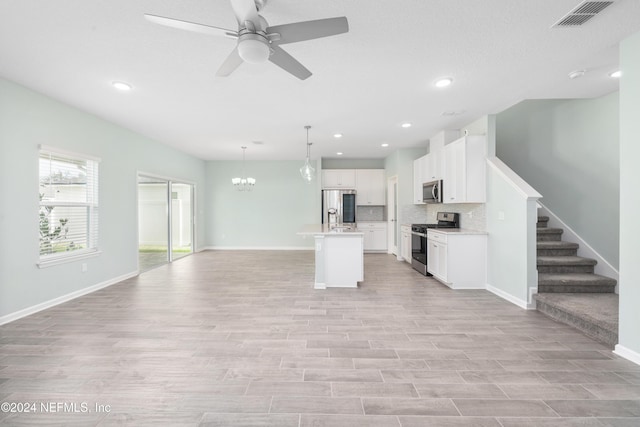 kitchen featuring white cabinetry, stainless steel appliances, pendant lighting, a center island with sink, and ceiling fan with notable chandelier