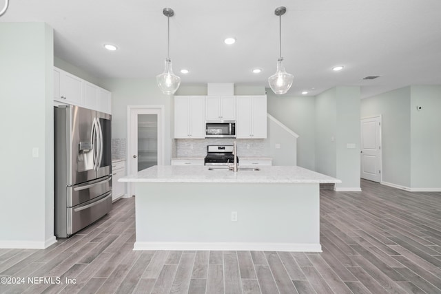 kitchen with pendant lighting, white cabinets, a center island with sink, decorative backsplash, and appliances with stainless steel finishes