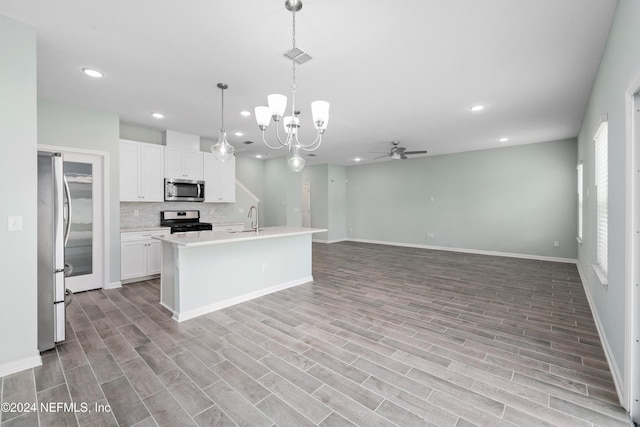 kitchen with appliances with stainless steel finishes, ceiling fan with notable chandelier, a center island with sink, white cabinetry, and hanging light fixtures