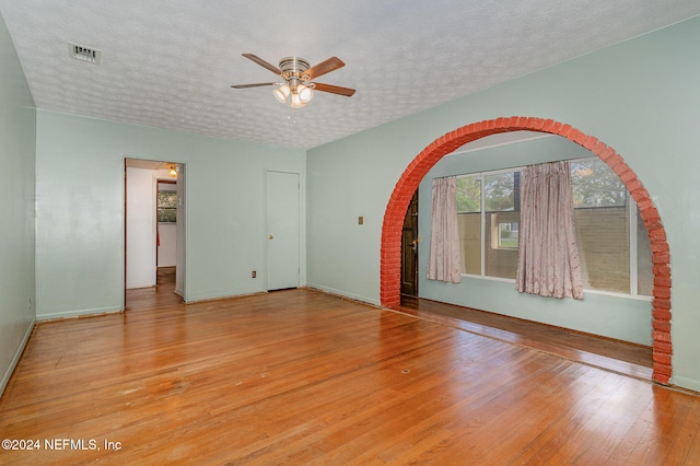 unfurnished room with a textured ceiling, light wood-type flooring, and ceiling fan