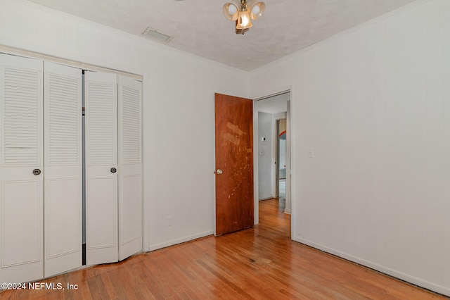 unfurnished bedroom featuring light wood-type flooring, a closet, and crown molding