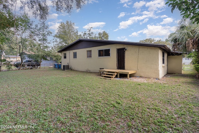 rear view of house with central AC unit and a yard