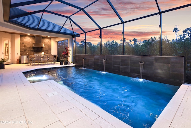 pool at dusk featuring pool water feature, glass enclosure, area for grilling, and a patio area