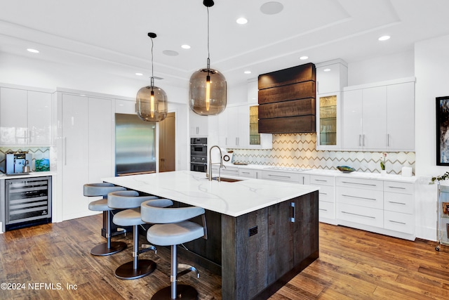 kitchen with dark wood-type flooring, premium range hood, sink, an island with sink, and beverage cooler