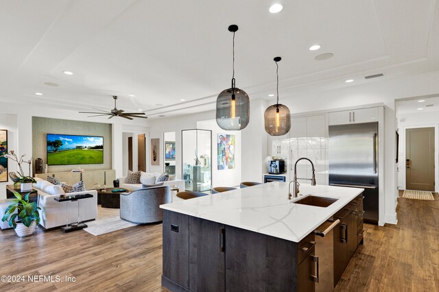 kitchen featuring sink, decorative light fixtures, white cabinets, built in refrigerator, and an island with sink