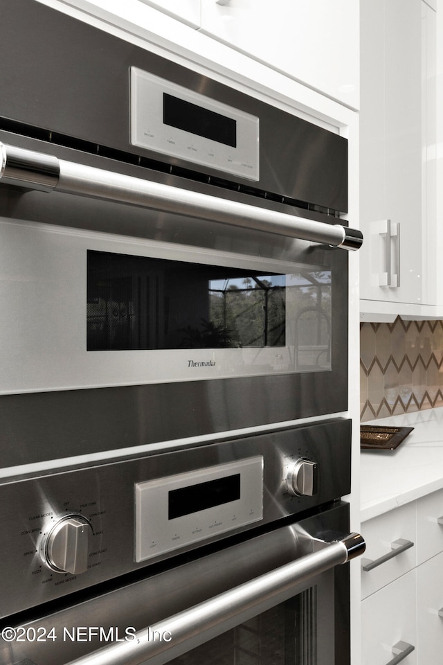 room details featuring backsplash, white cabinetry, and double oven