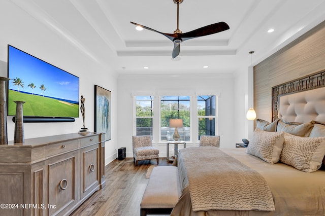 bedroom featuring ceiling fan, light hardwood / wood-style floors, and a tray ceiling