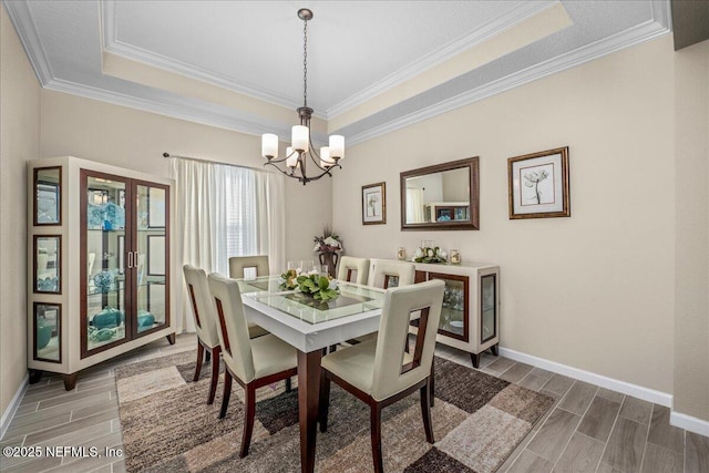 dining area featuring a raised ceiling, ornamental molding, and a chandelier