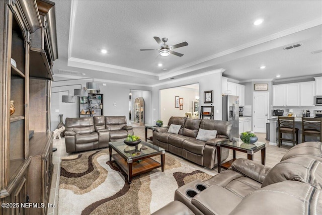 living room with crown molding, ceiling fan, a tray ceiling, and a textured ceiling