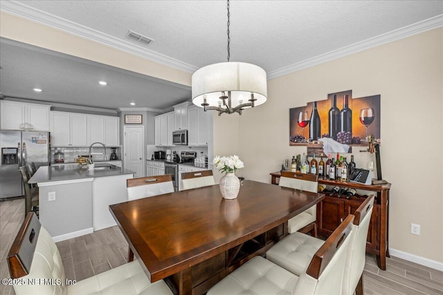 dining area featuring sink, crown molding, a chandelier, and a textured ceiling