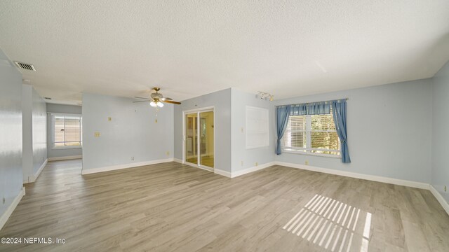 empty room featuring a wealth of natural light, ceiling fan, and light wood-type flooring