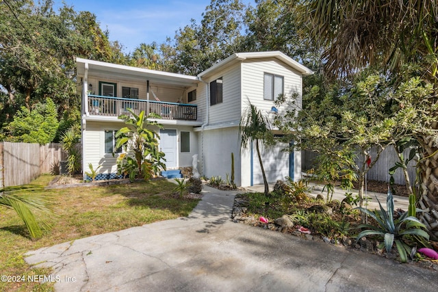 front facade with fence, a front yard, a garage, a balcony, and driveway