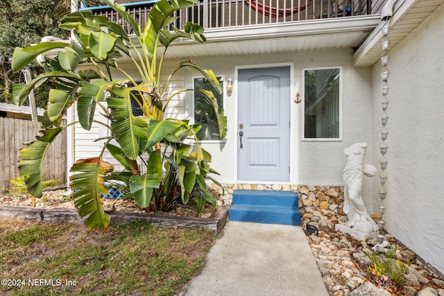 property entrance with stucco siding, a balcony, and fence