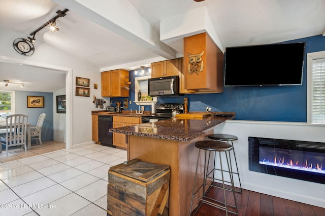 kitchen with kitchen peninsula, dark stone counters, a kitchen bar, light tile patterned floors, and black appliances