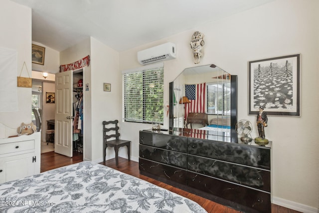 bedroom featuring a walk in closet, baseboards, wood finished floors, and a wall mounted AC