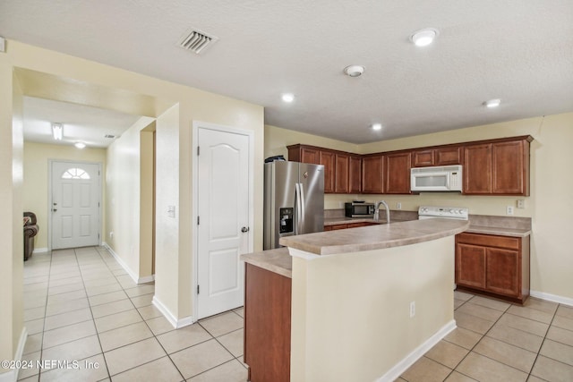 kitchen featuring a textured ceiling, light tile patterned floors, an island with sink, and white appliances