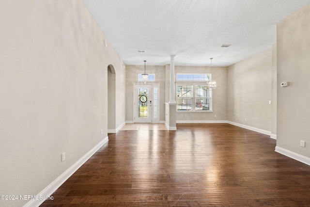 unfurnished living room featuring a textured ceiling, an inviting chandelier, and dark wood-type flooring