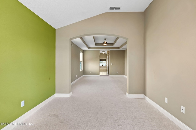 hall with a raised ceiling, lofted ceiling, and light carpet