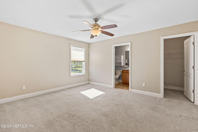 unfurnished bedroom with ensuite bath, ceiling fan, light colored carpet, and a spacious closet