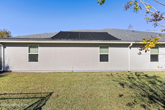 back of property featuring a lawn and solar panels