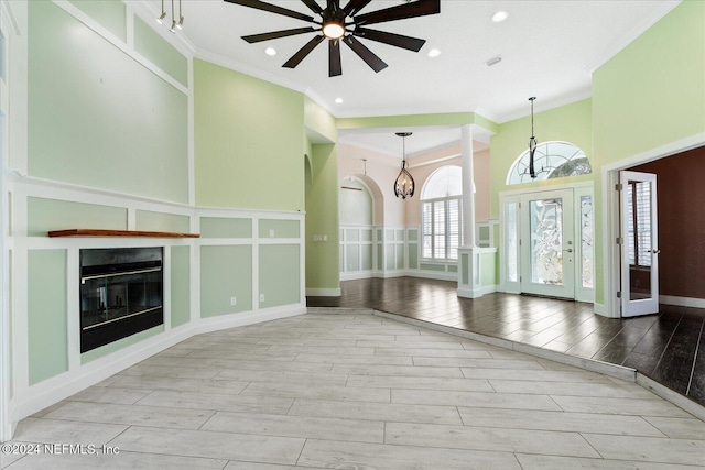 unfurnished living room with a high ceiling, light wood-type flooring, ceiling fan, and ornamental molding