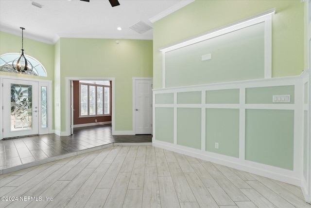 foyer entrance with a towering ceiling, light wood-type flooring, ceiling fan with notable chandelier, and crown molding