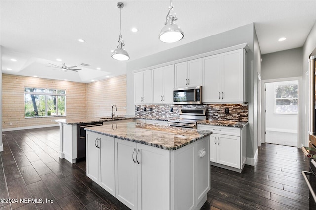 kitchen with white cabinetry, kitchen peninsula, appliances with stainless steel finishes, hanging light fixtures, and a center island