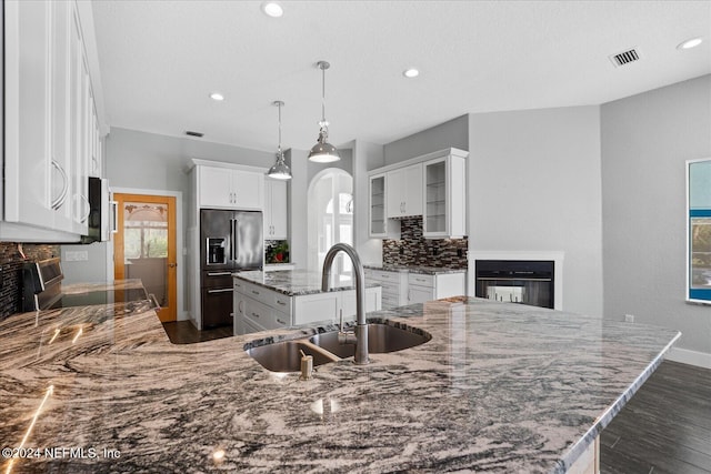 kitchen with light stone counters, stainless steel appliances, white cabinetry, sink, and a kitchen island with sink