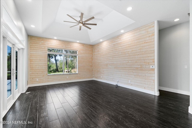 empty room with wood walls, dark hardwood / wood-style floors, ceiling fan, and a tray ceiling