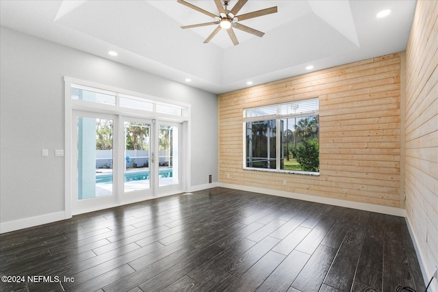 empty room featuring dark hardwood / wood-style floors, ceiling fan, wooden walls, and a raised ceiling