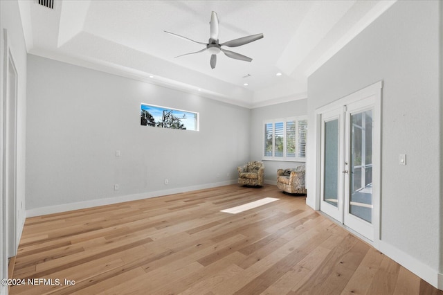 empty room with french doors, light hardwood / wood-style floors, ceiling fan, and a tray ceiling