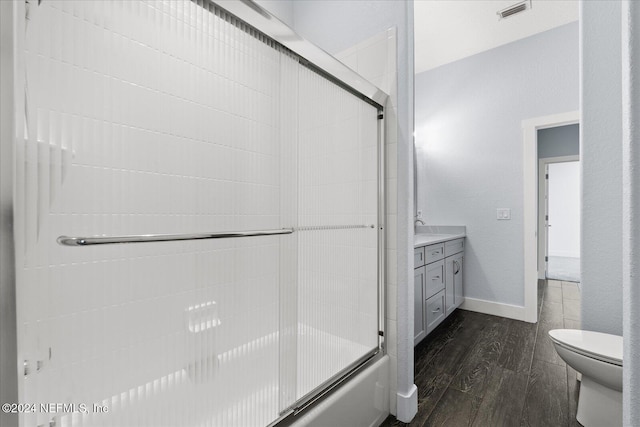 full bathroom with shower / bath combination with glass door, hardwood / wood-style flooring, vanity, and toilet