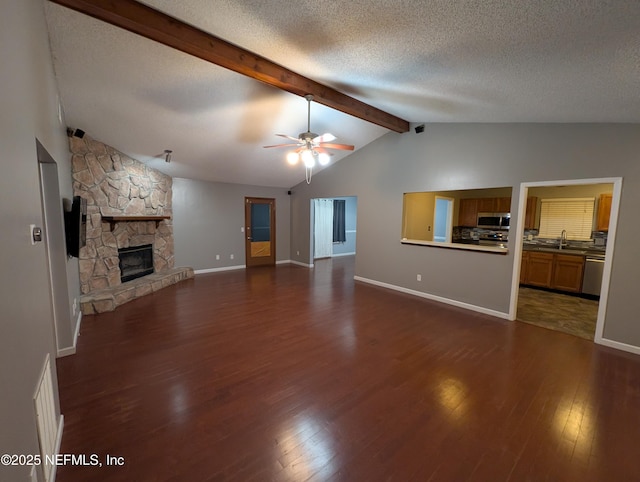 unfurnished living room with a stone fireplace, lofted ceiling with beams, ceiling fan, dark wood-type flooring, and a textured ceiling